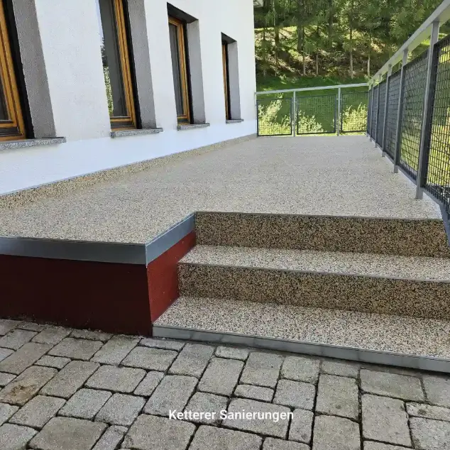 Drei frisch sanierte Stufen, die nahtlos und fugenlos in eine modernisierte Terrassenfläche mit Steinteppich übergehen